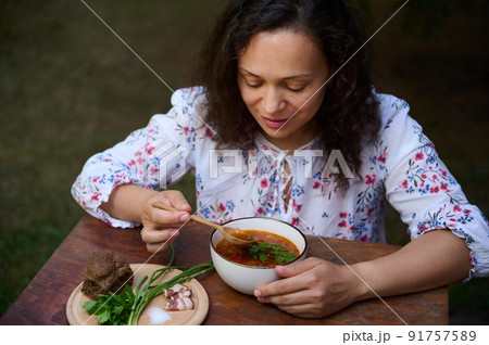 Cute woman tastes Ukrainian dish- Borscht served with sliced bacon, whole grain rye bread, green onion on wooden board 91757589