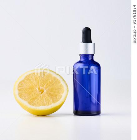 Blue glass bottle with pipette, next to it is half a lemon on a white front. 91761834