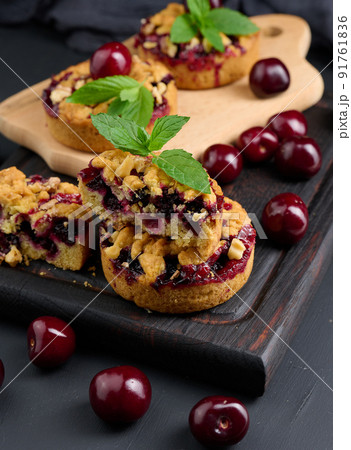 Portion crumble pie with cherries on a wooden board decorated with green mint leaves Portion crumble pie with cherries on a wooden board decorated with green mint leaves 91761836