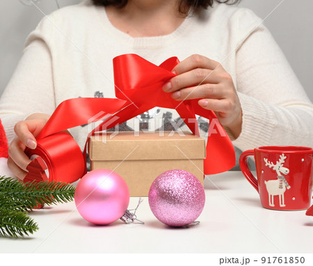 woman in a white sweater sits at the table and wraps gifts for Christmas. Preparing for the holidays 91761850