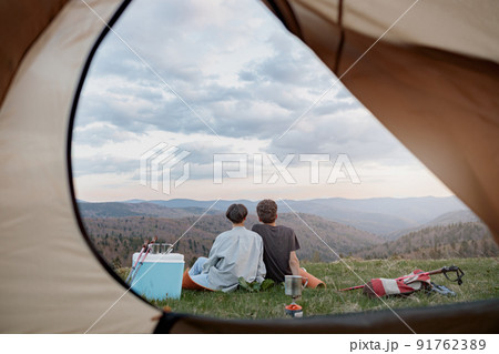 View from inside tent on beautiful landscape of mountains and couple resting. Love and travel. View from inside tent on beautiful landscape of mountains and couple resting. Love and travel. 91762389