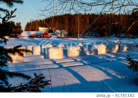 A winter country landscape with hay bales and hare tracks on snowy field in sunset. 91785382