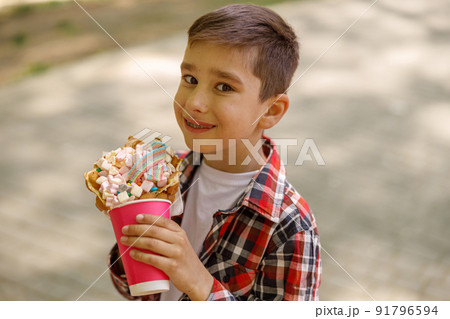 Portrait of cute small Caucasian boy with sweet waffle in hands. Kid smiling with fast food. Portrait of cute small Caucasian boy with sweet waffle in hands. Kid smiling with fast food. 91796594