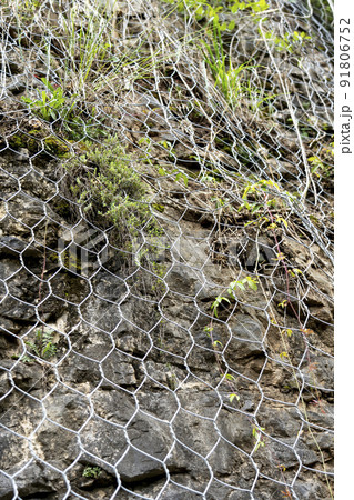 Natural rock with mesh to protect against landslides dangerously sliding down the cliff onto the road. Rockfall and falling stones protection Natural rock with mesh to protect against landslides dangerously sliding down the cliff onto the road. Rockfall and falling stones protection 91806752
