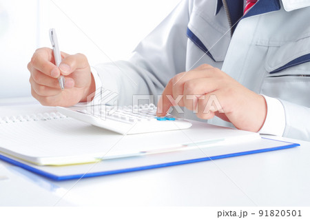 電卓で計算をする作業服姿の男性 91820501