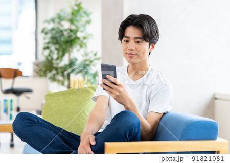 リビングでスマホを見る若い男性 91821081