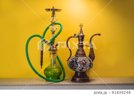 hookah shisha with glass flask and metal bowl with colored smoke on a yellow background. Traditional Eastern vacation for relaxation 91839248