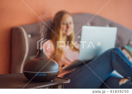 A woman sits on a bed and works on a laptop. Aroma diffuser next to the bed 91839250