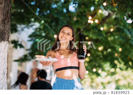 Young woman carries a plate of snacks and a drink in hands Young woman carries a plate of snacks and a drink in hands 91839925