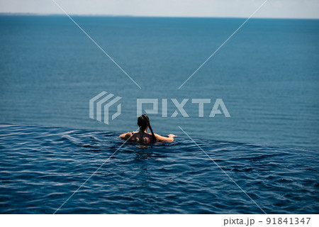 Happy woman in swimsuit swimming in infinity pool against seafront. Happy woman in swimsuit swimming in infinity pool against seafront. 91841347