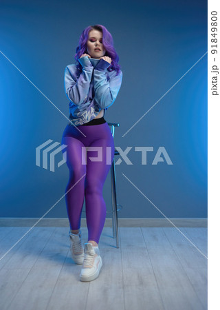 a girl in stylish purple sportswear and with purple hair poses sexually on a bar stool 91849800