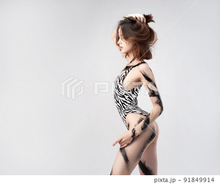 slender girl in a spotted bodysuit swimwear painted with spots of black paint on a white background 91849914
