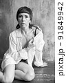 A girl with a sensual face and eyes in a white shirt and with a bare shoulder is sitting on a wooden floor. 91849942