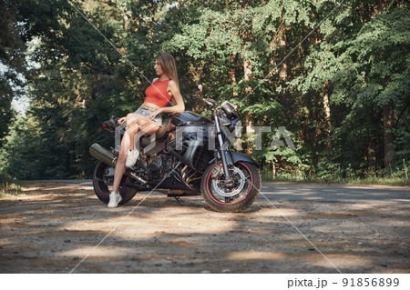 Young sexy woman biker sitting on a motorcycle on the side of a forest road 91856899