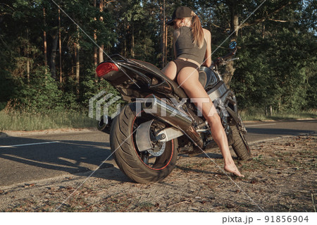 Young sexy woman biker in bikini sitting on a motorcycle on the side of a forest road 91856904