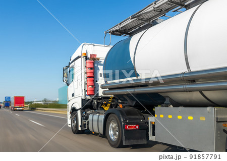 White big modern tanker shipment cargo commercial semi trailer truck moving fast on motorway road city urban suburb. Business distribution logistics service. Lorry driving highway sunny day 91857791