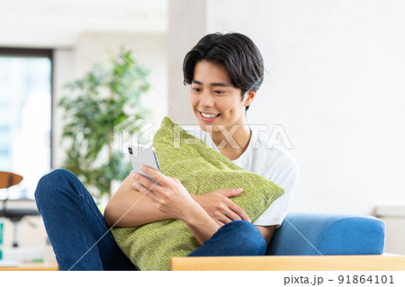 リビングでスマホを見る若い男性 91864101