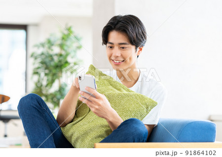 リビングでスマホを見る若い男性 91864102