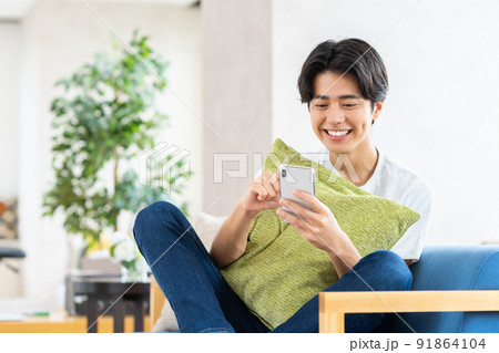 リビングでスマホを見る若い男性 91864104