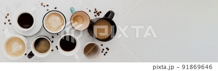 Top view on flat lay with many different full and empty coffee cups composition on gray white concrete background. Variety of tea mug collection layout. Dried coffee beans. Espresso, latte, americano Top view on flat lay with many different full and empty coffee cups composition on gray white concrete background. Variety of tea mug collection layout. Dried coffee beans. Espresso, latte, americano 91869646