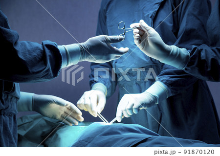 doctor and nurse medical team are performing surgical operation at emergency room in hospital. assistant hands out scissor and instruments to surgeons during operation. 91870120