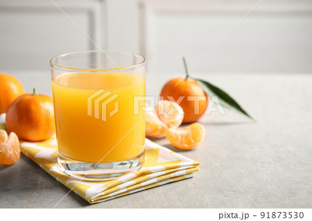 Glass of fresh tangerine juice and fruits on light grey table. Space for text Glass of fresh tangerine juice and fruits on light grey table. Space for text 91873530