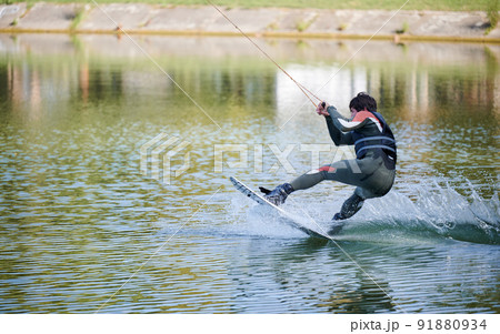 Wakeboarder surfing on lake. Young man surfer having fun wakeboarding in the cable park. Water sport, outdoor activity concept. 91880934