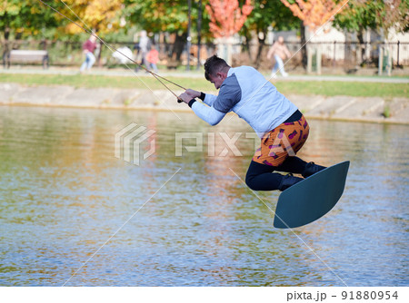 Wakeboarder surfing on lake. Young man surfer having fun wakeboarding in the cable park. Water sport, outdoor activity concept. Wakeboarder surfing on lake. Young man surfer having fun wakeboarding in the cable park. Water sport, outdoor activity concept. 91880954