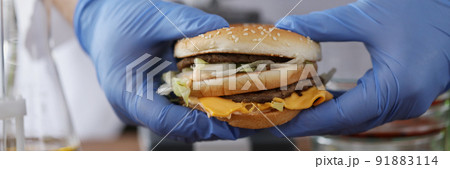 Male chemist holding tasty burger in hand with blue protective glove Male chemist holding tasty burger in hand with blue protective glove 91883114