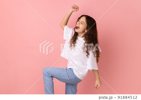 Happy satisfied little girl wearing white T-shirt showing yes gesture and screaming celebrating her victory, success, dreams comes true, euphoria. Indoor studio shot isolated on pink background. Happy satisfied little girl wearing white T-shirt showing yes gesture and screaming celebrating her victory, success, dreams comes true, euphoria. Indoor studio shot isolated on pink background. 91884512