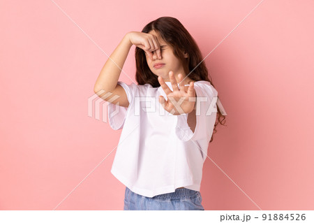 Awful smell. Confused little girl wearing white T-shirt pinching her nose to hold breath and showing stop gesture, disgusted by unpleasant odor, fart. Indoor studio shot isolated on pink background. 91884526
