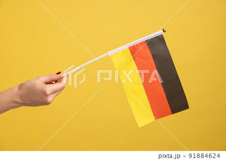 Profile side view closeup of woman hand holding Germany flag. Day of Germany - 3th October. Indoor studio shot isolated on yellow background. 91884624