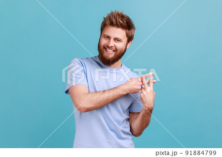 Internet trends. Portrait of satisfied smiling bearded man crossing fingers to make hashtag sign and looking at camera with toothy smile. Indoor studio shot isolated on blue background. 91884799