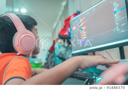 Asian kid is coding and scripting program on on his game streaming desktop computer with headphone on. Asian kid is coding and scripting program on on his game streaming desktop computer with headphone on. 91886370