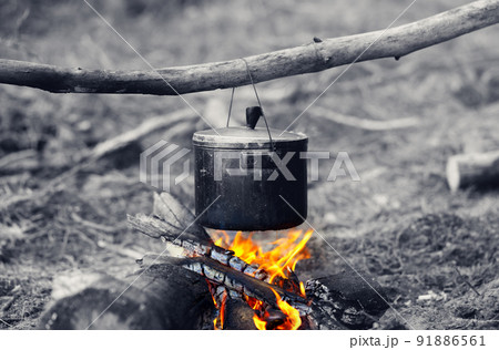 Cooking in sooty cauldron on campfire at forest. Black and white selective color effect. 91886561