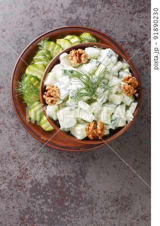 Bulgarian Snezhanka salad or Snow White salad which is made of strained yogurt, cucumber, garlic, salt, usually cooking oil, dill, walnuts close-up in a bowl. Vertical top view 91890230