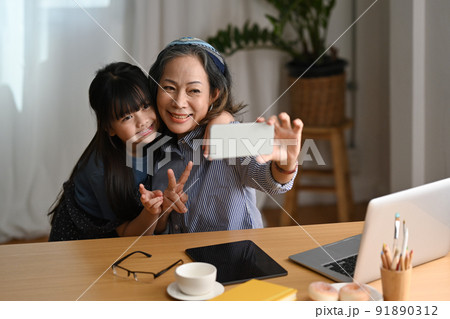 Happy grandmother and cute little grandchild having fun taking selfie on smart phone at home 91890312