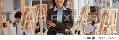 Portrait of smiling female arfican american teacher in modern classroom with kids drawing lesson in background Portrait of smiling female arfican american teacher in modern classroom with kids drawing lesson in background 91891647