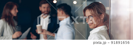 Mature smiling business lady at office with group of colleagues on background, working on laptop 91891656