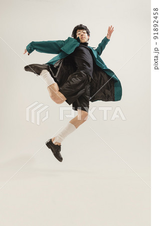 Portrait of stylish young man in black outfit and green coat posing isolated over grey studio background. Looks delightful Portrait of stylish young man in black outfit and green coat posing isolated over grey studio background. Looks delightful 91892458