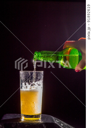 With a feminine hand, She poured cold beer with beer bubbles and foam into a glass. The dark key. Black background. Oktoberfestbier 91892619