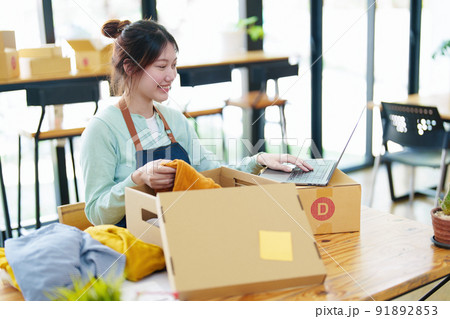 Portrait of a small startup business, SME owner, Asian female entrepreneur, talks to via video conferance, lets customers see products before pricing and packing them into boxes. Online Business. 91892853