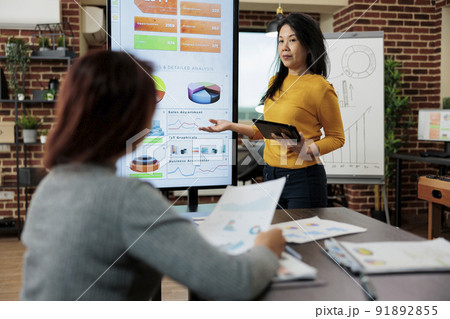 Executive manager showing company graphs using vertical monitor discussing business strategy with entrepreneur woman in startup office. Management team analyzing marketing statistics 91892855