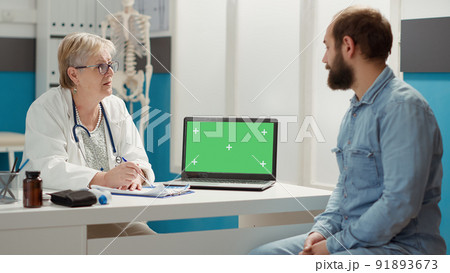 Senior doctor and patient looking at laptop with greenscreen at checkup visit. Man and woman using isolated template with blank chromakey background and mockup copyspace on display. Senior doctor and patient looking at laptop with greenscreen at checkup visit. Man and woman using isolated template with blank chromakey background and mockup copyspace on display. 91893673