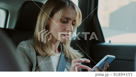 Beautiful woman typing on her smartphone in the car. Lady manager looking at phone in the back seat of a car. Beautiful woman typing on her smartphone in the car. Lady manager looking at phone in the back seat of a car. 91894355