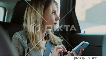 Beautiful woman typing on her smartphone in the car. Lady manager looking at phone in the back seat of a car. 91894356