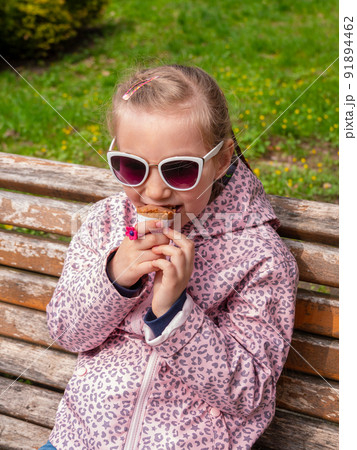 Pretty little girl eating an ice cream in a waffle cone outdoor. Child in sunglasses with chocolate gelato in green park 91894462