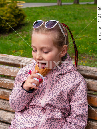 Pretty little girl eating an ice cream in a waffle cone outdoor. Child in sunglasses with chocolate gelato in green park 91894464