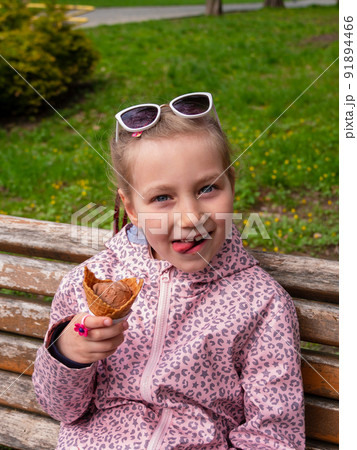 Pretty little girl eating an ice cream in a waffle cone outdoor. Child in sunglasses with chocolate gelato in green park 91894466