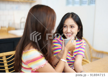 lgbtq, LGBT concept, homosexuality, portrait of two Asian women posing happy together and showing love for each other while having coffee at the dining table. 91894715